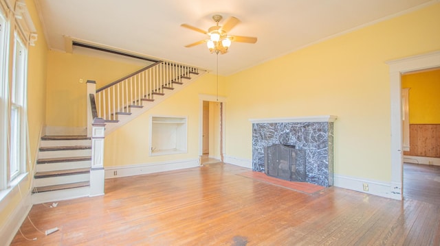 unfurnished living room featuring ceiling fan, wood-type flooring, ornamental molding, and a high end fireplace