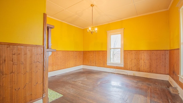 spare room featuring dark hardwood / wood-style floors, ornamental molding, wooden walls, and a chandelier