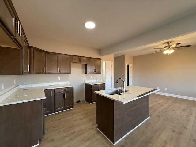 kitchen with dark brown cabinetry, light wood-style flooring, a kitchen island with sink, and a sink