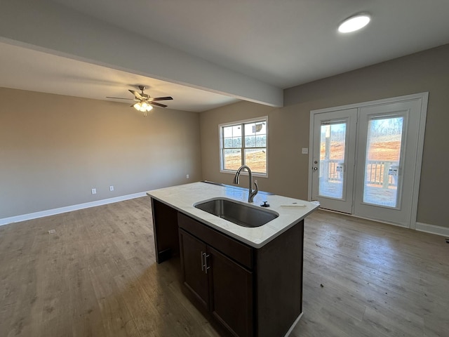 kitchen featuring a kitchen island with sink, wood finished floors, a sink, open floor plan, and light countertops