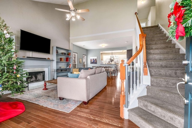 living room featuring hardwood / wood-style floors, ceiling fan with notable chandelier, a premium fireplace, and a towering ceiling