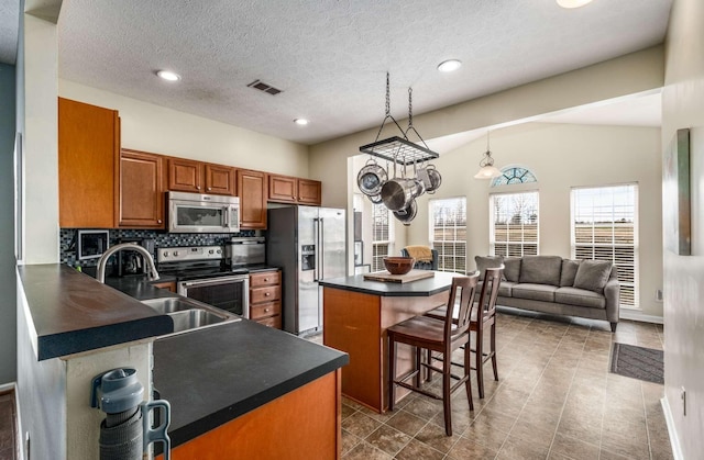 kitchen featuring lofted ceiling, backsplash, hanging light fixtures, a kitchen bar, and stainless steel appliances