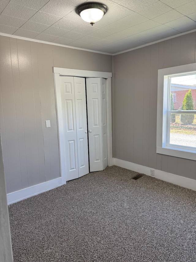 unfurnished bedroom with carpet flooring, wooden walls, and a closet