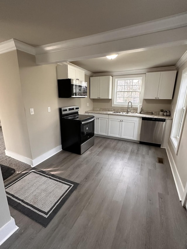 kitchen with crown molding, sink, appliances with stainless steel finishes, white cabinetry, and wood-type flooring