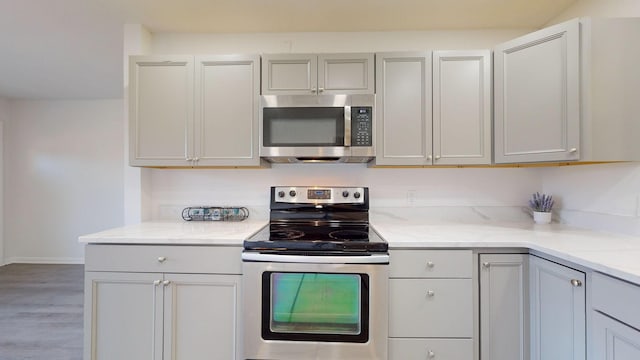 kitchen featuring gray cabinetry, light stone counters, light hardwood / wood-style flooring, and appliances with stainless steel finishes