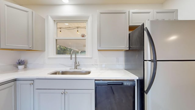 kitchen featuring light stone counters, sink, black dishwasher, gray cabinets, and stainless steel refrigerator