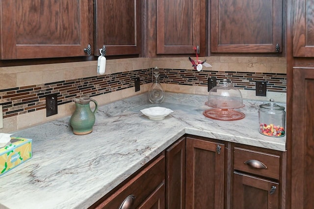 kitchen featuring dark brown cabinetry, light stone countertops, and backsplash