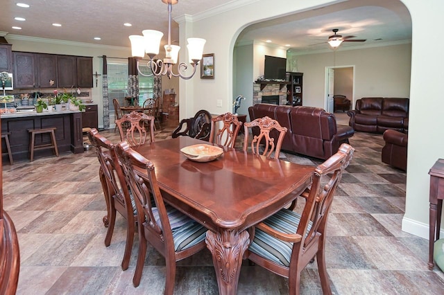 dining space with ceiling fan with notable chandelier, crown molding, and a fireplace