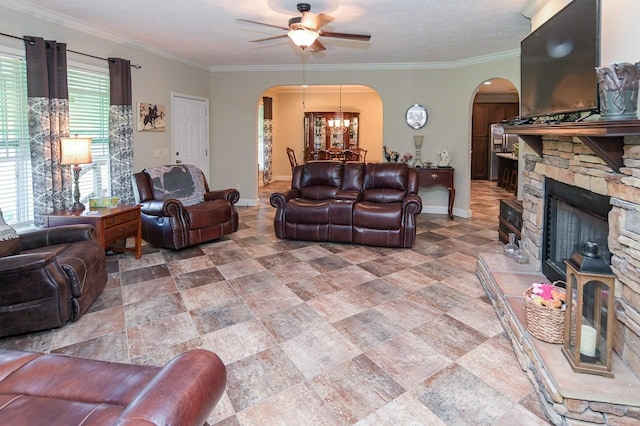 living room featuring ceiling fan with notable chandelier, a stone fireplace, and crown molding