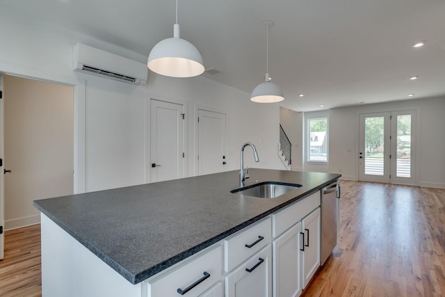 kitchen with a wall mounted AC, a kitchen island with sink, sink, decorative light fixtures, and white cabinets