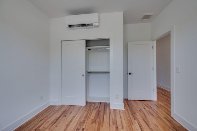 unfurnished bedroom featuring an AC wall unit, a closet, and light hardwood / wood-style flooring