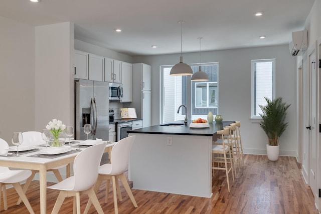 kitchen with a wall mounted air conditioner, appliances with stainless steel finishes, sink, white cabinets, and light hardwood / wood-style floors