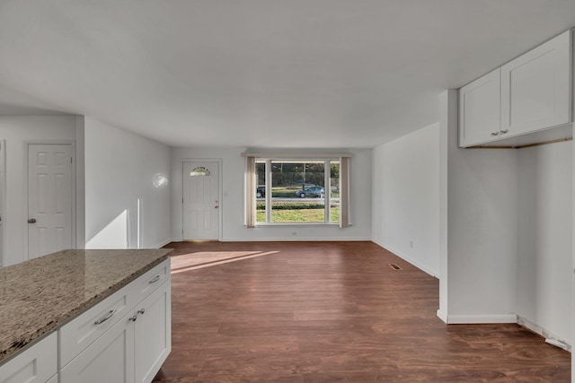 kitchen with light stone countertops, white cabinetry, and dark wood-type flooring