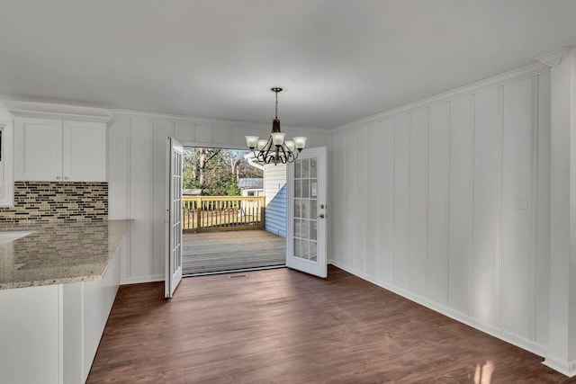 unfurnished dining area featuring crown molding, french doors, dark hardwood / wood-style floors, and an inviting chandelier