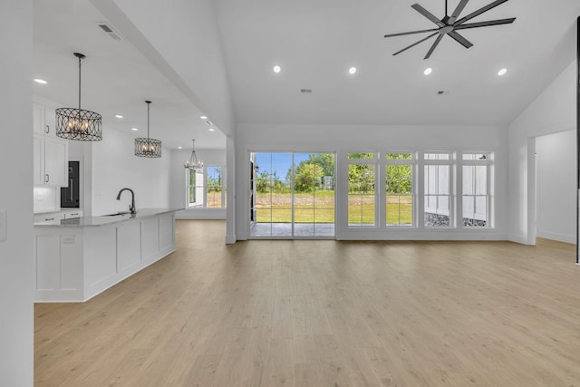 unfurnished living room with ceiling fan, light wood-type flooring, sink, and high vaulted ceiling