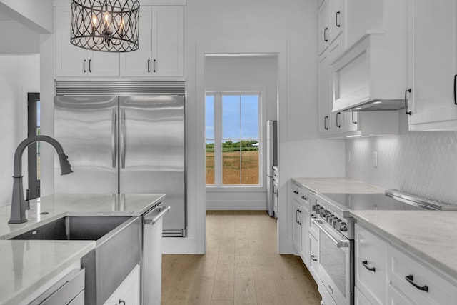 kitchen with high end appliances, white cabinets, hanging light fixtures, light stone countertops, and light hardwood / wood-style floors