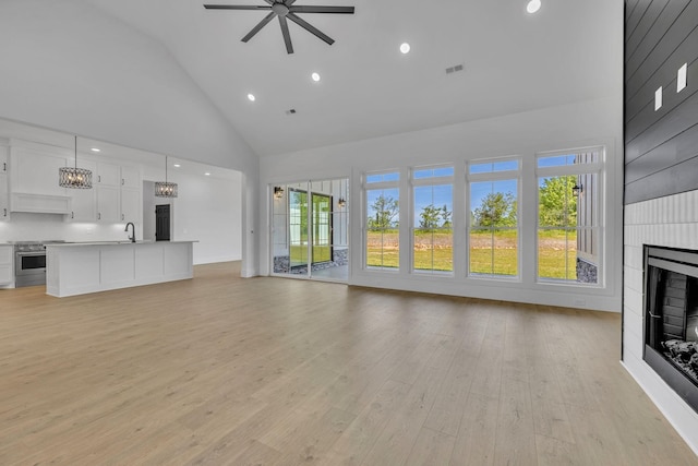 unfurnished living room with light wood-type flooring, a large fireplace, high vaulted ceiling, and ceiling fan