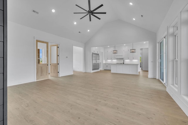 unfurnished living room with ceiling fan with notable chandelier, light wood-type flooring, high vaulted ceiling, and sink