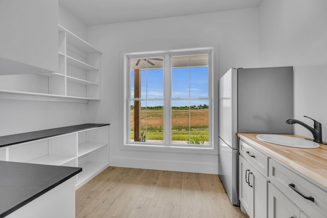 kitchen with stainless steel refrigerator, white cabinetry, sink, wooden counters, and light hardwood / wood-style floors