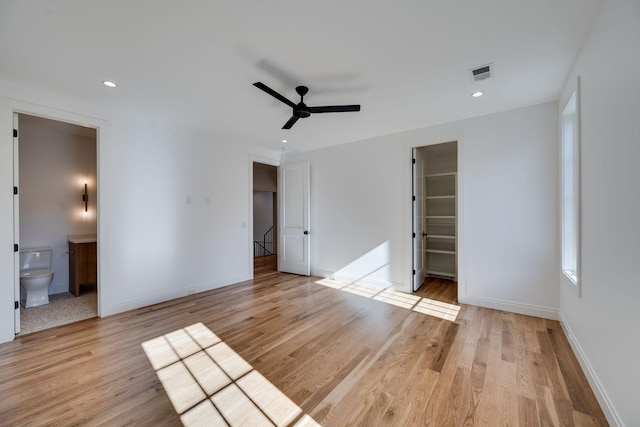 unfurnished bedroom featuring ensuite bathroom, a spacious closet, a closet, ceiling fan, and light hardwood / wood-style floors