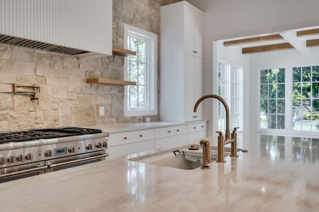 kitchen with sink, white cabinetry, light stone counters, beam ceiling, and decorative backsplash