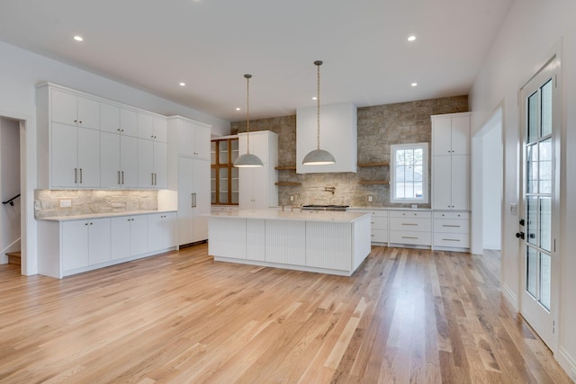 kitchen featuring hanging light fixtures, a spacious island, light hardwood / wood-style floors, white cabinets, and decorative backsplash