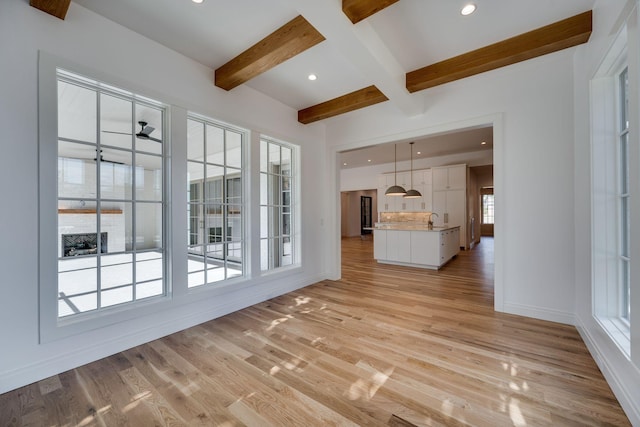 unfurnished living room with sink, light hardwood / wood-style floors, beamed ceiling, and ceiling fan