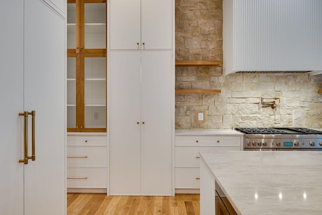 kitchen with light stone counters, light wood-type flooring, backsplash, white cabinets, and stove