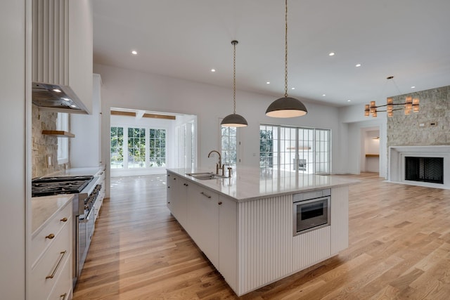 kitchen featuring decorative light fixtures, a kitchen island with sink, sink, and white cabinets