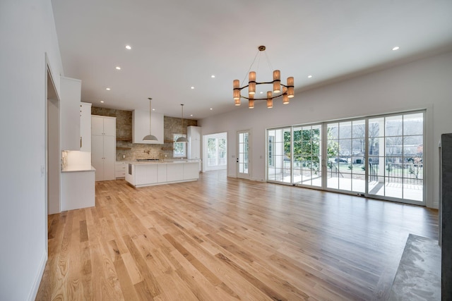 unfurnished living room with an inviting chandelier and light hardwood / wood-style floors