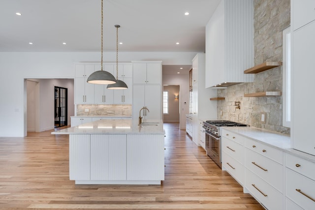 kitchen featuring light hardwood / wood-style flooring, white cabinetry, hanging light fixtures, high end stove, and an island with sink