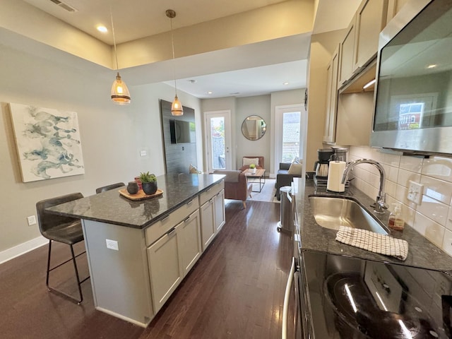 kitchen with sink, dark hardwood / wood-style floors, a kitchen island, and dark stone countertops