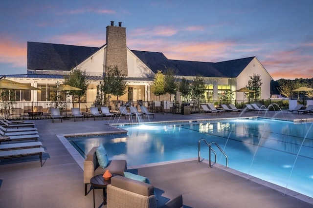 pool at dusk with pool water feature and a patio