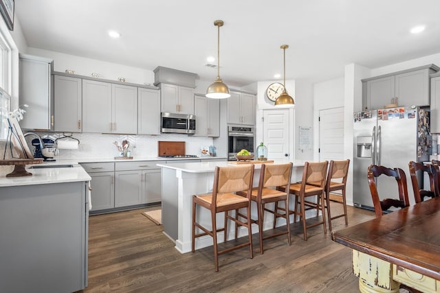 kitchen featuring appliances with stainless steel finishes, a kitchen island, hanging light fixtures, and dark wood-type flooring