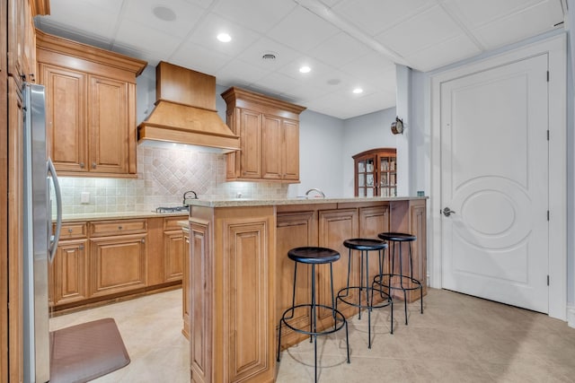 kitchen with appliances with stainless steel finishes, premium range hood, backsplash, a kitchen island, and a kitchen bar