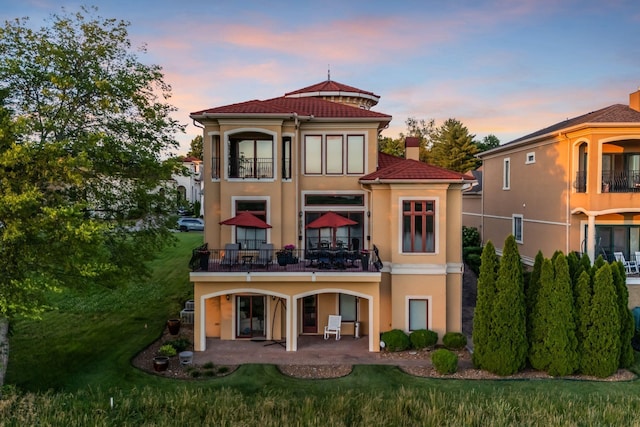 back house at dusk featuring a patio, a balcony, and a yard