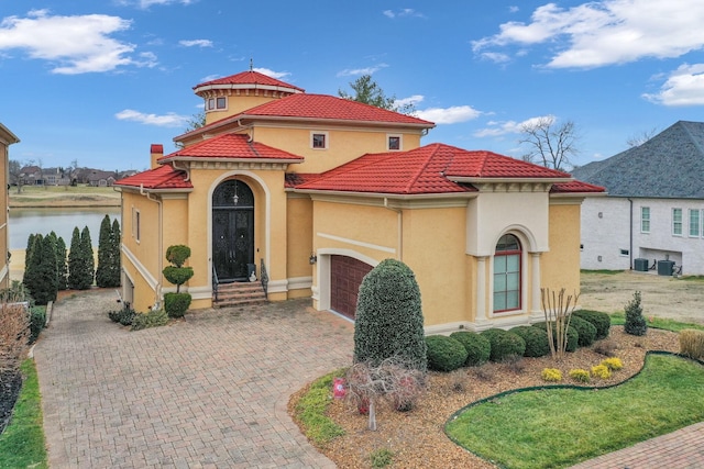 mediterranean / spanish-style house featuring central air condition unit, a water view, and a garage