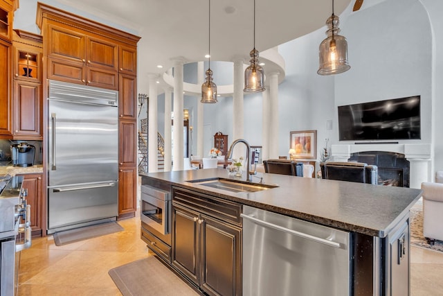 kitchen featuring an island with sink, decorative light fixtures, built in appliances, sink, and light tile patterned floors