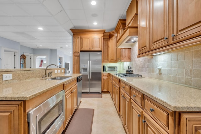 kitchen with sink, light stone countertops, stainless steel appliances, and premium range hood