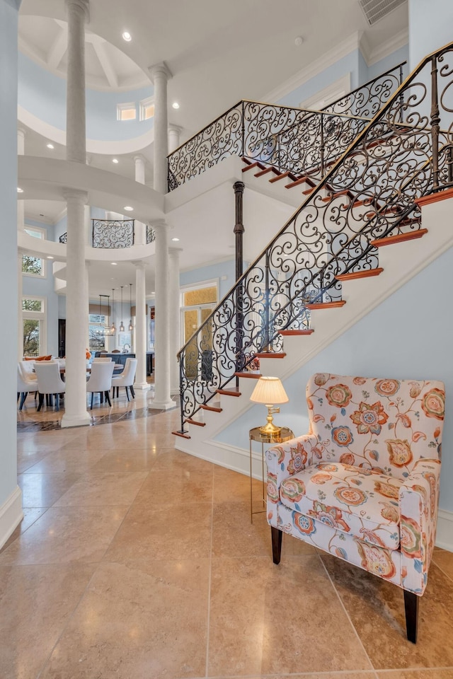 entrance foyer featuring decorative columns, ornamental molding, and a towering ceiling