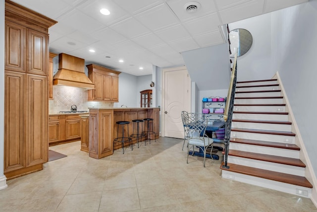 kitchen with stainless steel gas stovetop, a center island, backsplash, custom exhaust hood, and a kitchen bar