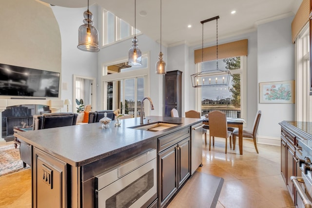 kitchen featuring sink, stainless steel microwave, hanging light fixtures, an island with sink, and dark brown cabinets