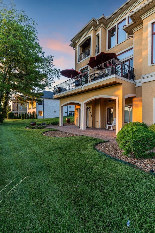 back house at dusk featuring a yard, a patio, and a balcony