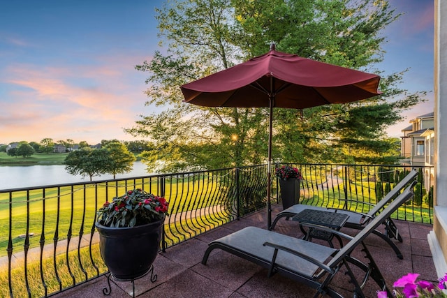 balcony at dusk featuring a water view