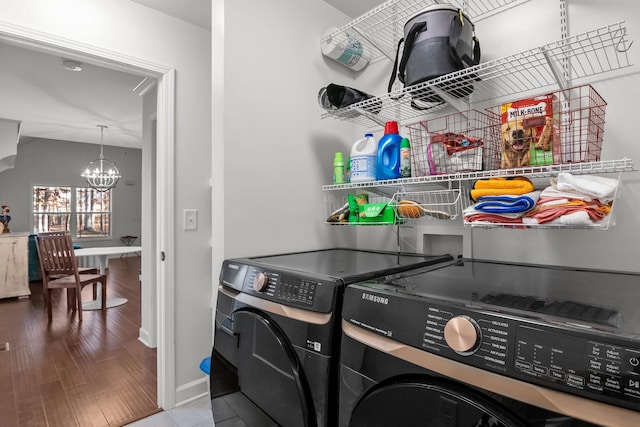 clothes washing area with washer and clothes dryer, a notable chandelier, and hardwood / wood-style flooring