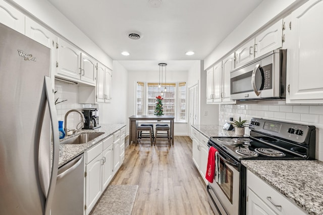 kitchen featuring appliances with stainless steel finishes, sink, decorative light fixtures, light hardwood / wood-style flooring, and white cabinetry