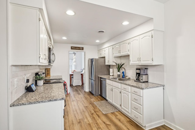 kitchen with white cabinetry, sink, light stone countertops, light wood-type flooring, and appliances with stainless steel finishes