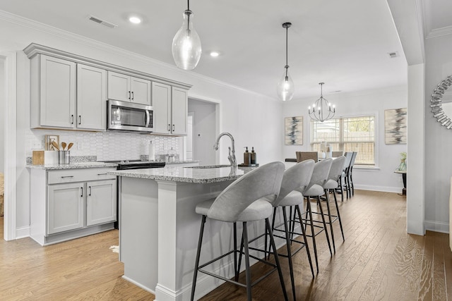 kitchen with a kitchen island with sink, sink, light stone countertops, and decorative light fixtures