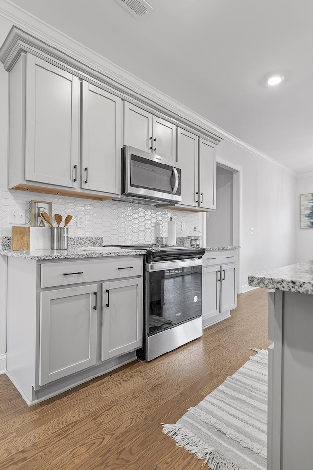 kitchen with tasteful backsplash, hardwood / wood-style floors, stainless steel appliances, and ornamental molding