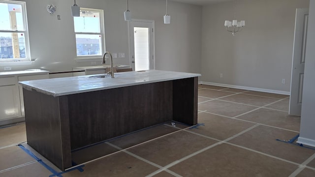 kitchen featuring pendant lighting, light tile patterned floors, white cabinets, an island with sink, and baseboards